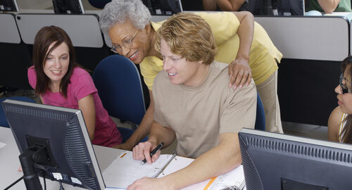 Teacher helping two students working in computer classroom