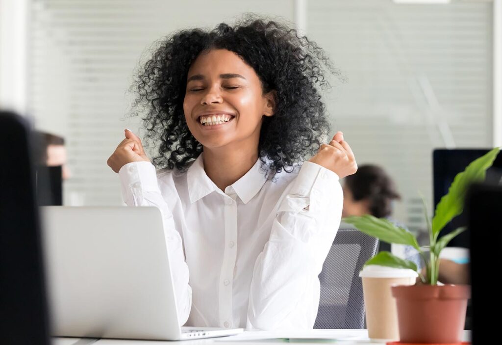 Young woman at desk with eyes closed smiling in triumph after outshining peers through use of Excel supplements